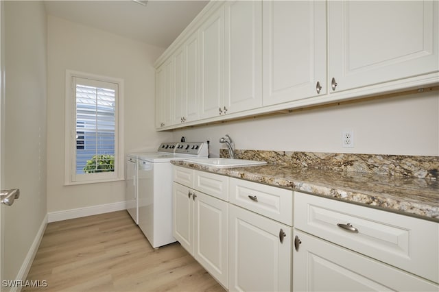 laundry area featuring sink, light hardwood / wood-style flooring, independent washer and dryer, and cabinets