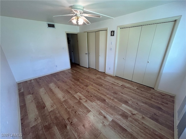 unfurnished bedroom featuring ceiling fan, multiple closets, and light hardwood / wood-style flooring