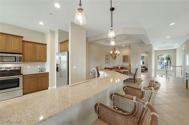 kitchen with light stone counters, tasteful backsplash, appliances with stainless steel finishes, a breakfast bar, and an inviting chandelier