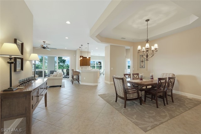 tiled dining area featuring ceiling fan with notable chandelier and a raised ceiling