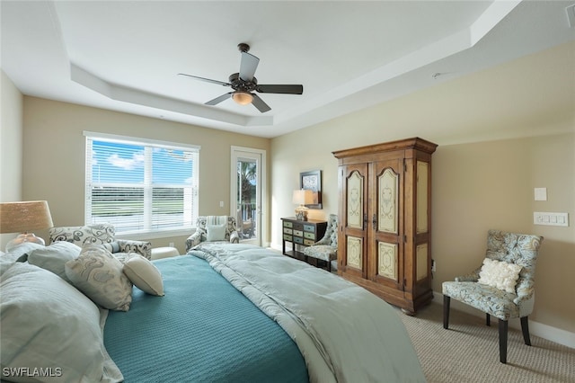 carpeted bedroom with ceiling fan and a tray ceiling