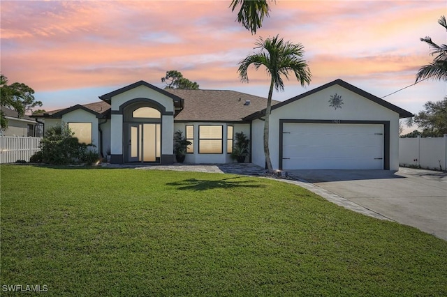 ranch-style house featuring a garage, fence, driveway, a yard, and stucco siding