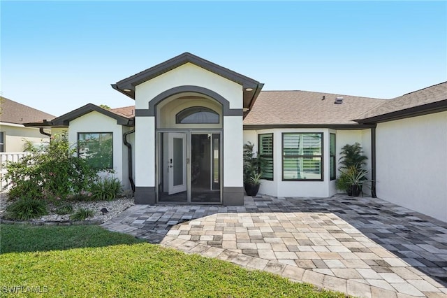 doorway to property featuring a lawn, a patio area, and stucco siding