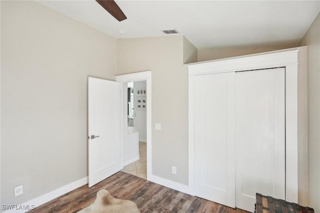 unfurnished bedroom with a closet, wood finished floors, visible vents, and baseboards