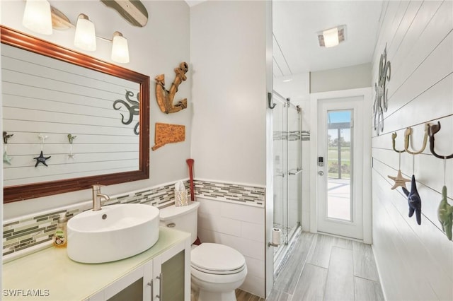 bathroom with tile walls, toilet, a stall shower, wainscoting, and vanity