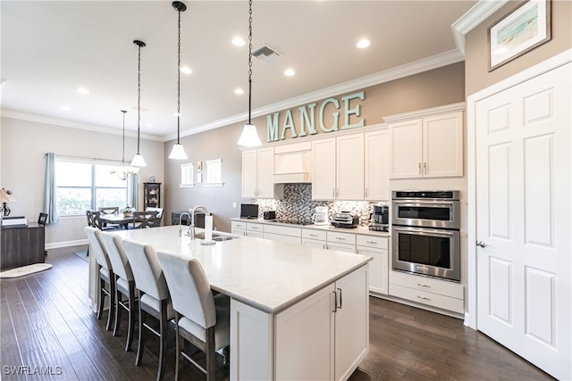 kitchen with stainless steel double oven, a center island with sink, dark hardwood / wood-style floors, and white cabinetry