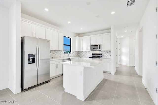 kitchen featuring white cabinets, a kitchen island, decorative backsplash, appliances with stainless steel finishes, and light tile patterned floors