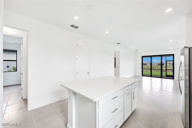 kitchen featuring light tile patterned floors, stainless steel fridge, white cabinetry, and a kitchen island