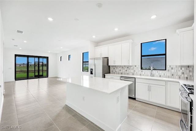 kitchen with sink, white cabinets, a kitchen island, decorative backsplash, and appliances with stainless steel finishes