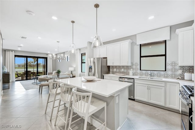 kitchen featuring hanging light fixtures, a kitchen island, backsplash, white cabinetry, and appliances with stainless steel finishes