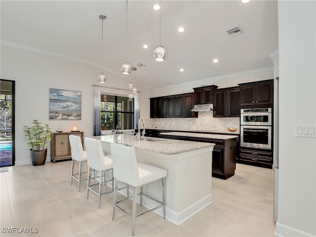 kitchen with pendant lighting, lofted ceiling, sink, an island with sink, and double oven