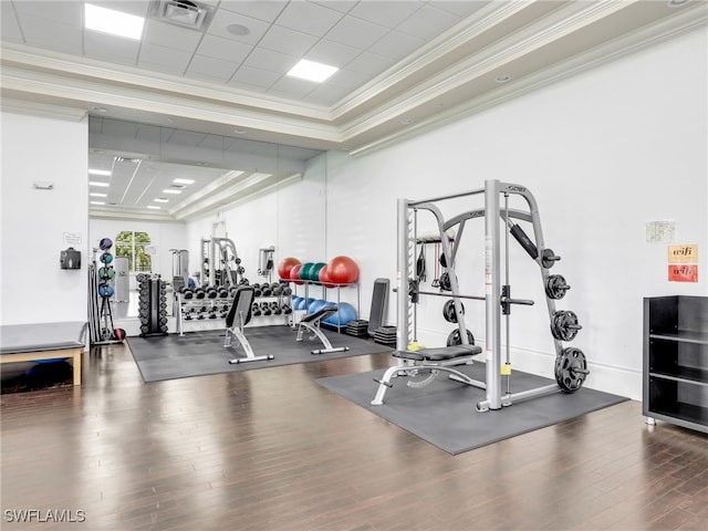 exercise room featuring hardwood / wood-style floors, a raised ceiling, and ornamental molding