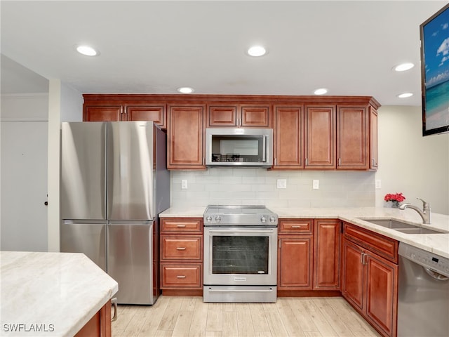 kitchen with appliances with stainless steel finishes, backsplash, light stone countertops, light hardwood / wood-style flooring, and sink