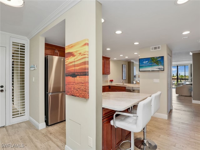 kitchen featuring a kitchen breakfast bar, kitchen peninsula, stainless steel appliances, light wood-type flooring, and crown molding