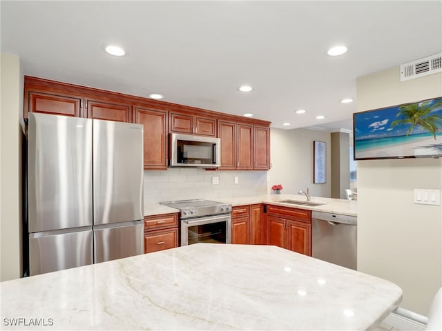 kitchen with tasteful backsplash, sink, kitchen peninsula, appliances with stainless steel finishes, and light stone countertops