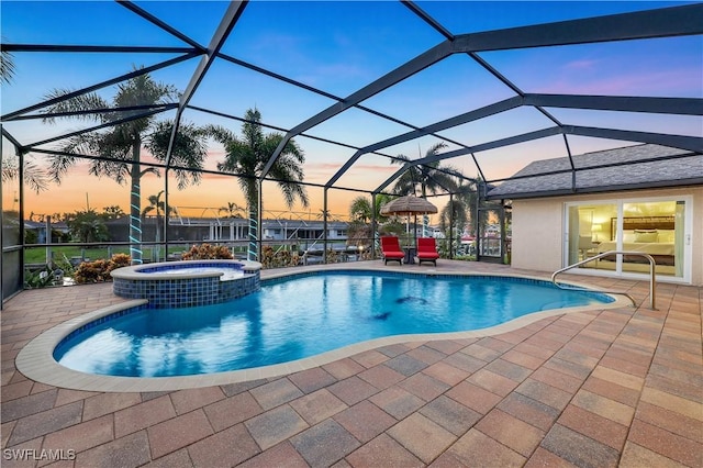 pool at dusk with a pool with connected hot tub, glass enclosure, and a patio