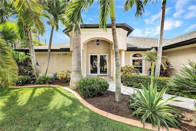 doorway to property with a yard, french doors, a shingled roof, and stucco siding