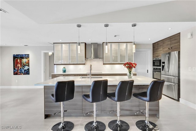 kitchen with stainless steel fridge, glass insert cabinets, light countertops, wall chimney range hood, and a sink