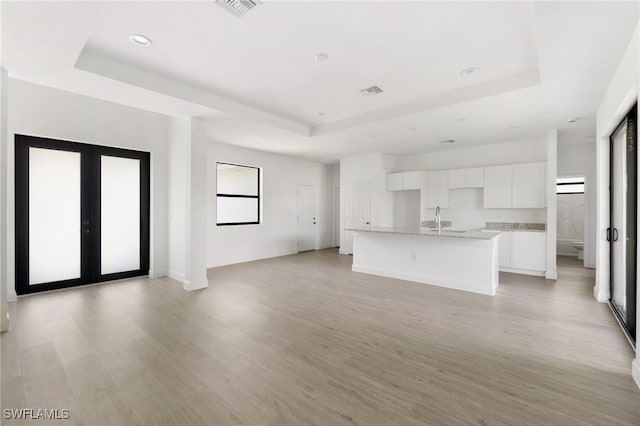 unfurnished living room featuring light wood-type flooring, a raised ceiling, and plenty of natural light