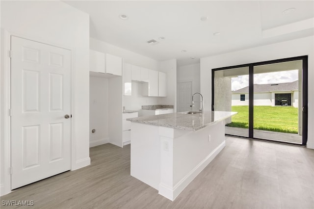 kitchen with light stone counters, sink, a center island with sink, white cabinetry, and light hardwood / wood-style floors