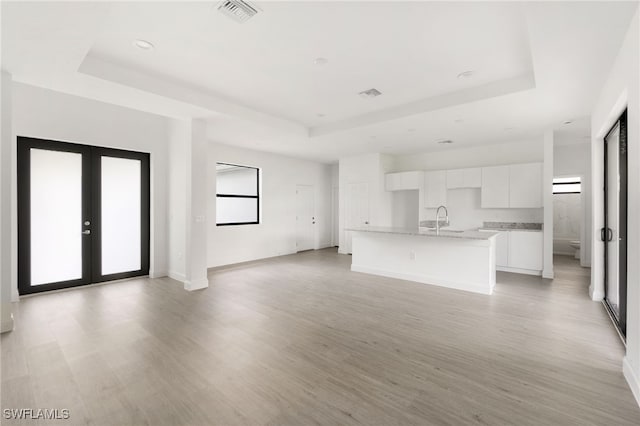 unfurnished living room with light wood-type flooring, a raised ceiling, and plenty of natural light