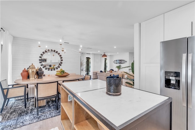 kitchen with white cabinetry, light hardwood / wood-style floors, a kitchen island, and stainless steel fridge with ice dispenser