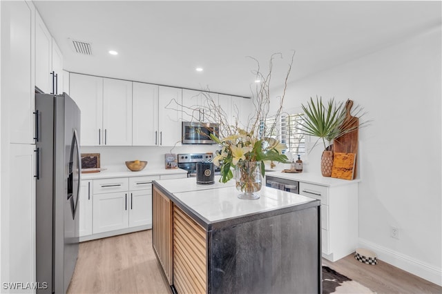 kitchen with white cabinets, a center island, appliances with stainless steel finishes, and light wood-type flooring