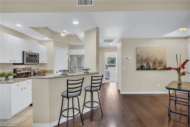 kitchen with white cabinets, stainless steel appliances, wood-type flooring, and a center island with sink