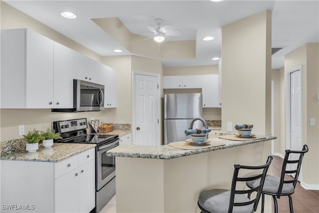 kitchen with white cabinets, a kitchen bar, stainless steel appliances, and light hardwood / wood-style flooring