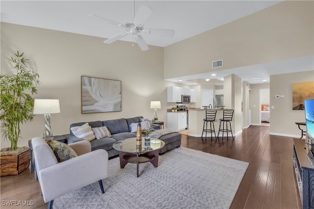 living room featuring ceiling fan, dark hardwood / wood-style floors, and a towering ceiling