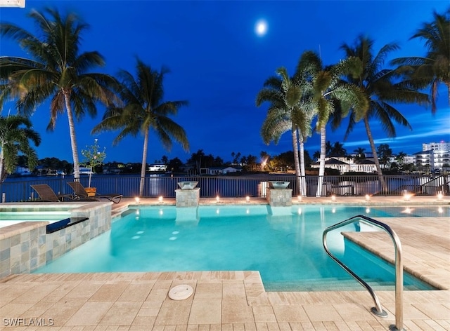 pool at night featuring pool water feature, an in ground hot tub, and a patio