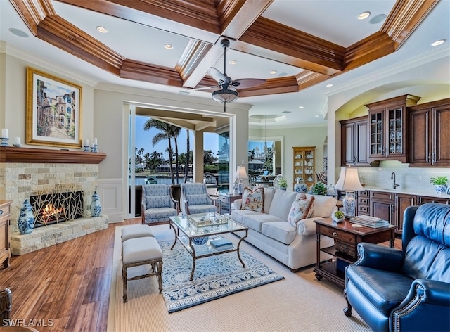 living room with coffered ceiling, ceiling fan, crown molding, a fireplace, and light hardwood / wood-style floors