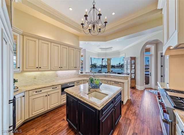 kitchen with light stone counters, dark hardwood / wood-style floors, kitchen peninsula, cream cabinetry, and a center island with sink