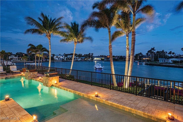 pool at dusk featuring a water view and a patio