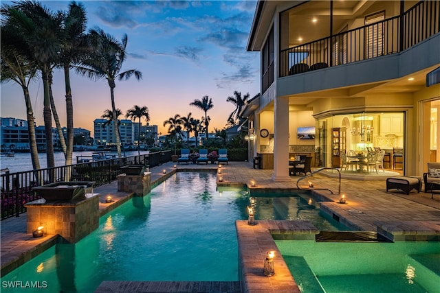 pool at dusk with a water view, area for grilling, and a patio area