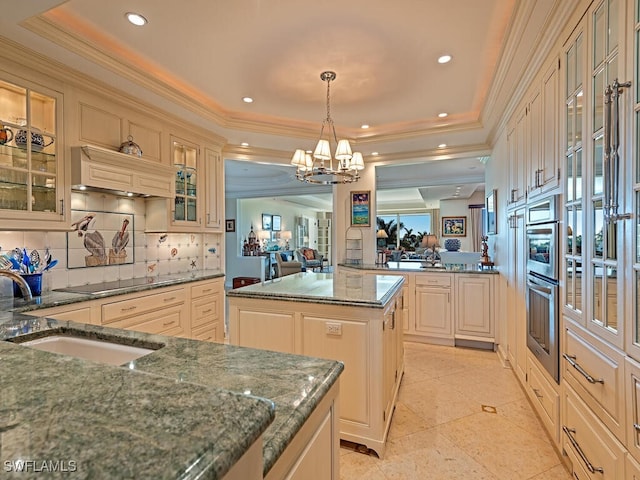 kitchen featuring a tray ceiling, a center island, sink, and decorative light fixtures