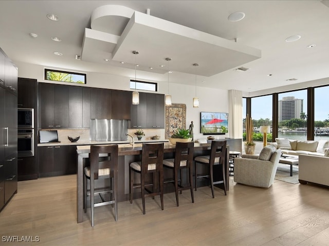 kitchen featuring a kitchen bar, tasteful backsplash, light hardwood / wood-style flooring, hanging light fixtures, and an island with sink