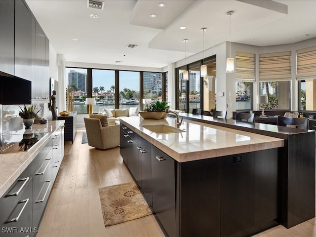 kitchen with sink, pendant lighting, a spacious island, black electric cooktop, and light wood-type flooring