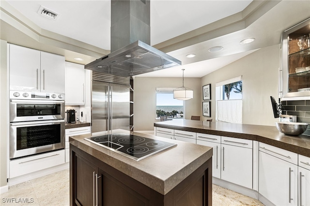 kitchen featuring appliances with stainless steel finishes, tasteful backsplash, island range hood, white cabinetry, and hanging light fixtures