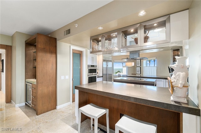 kitchen with a breakfast bar, white cabinets, wine cooler, appliances with stainless steel finishes, and kitchen peninsula