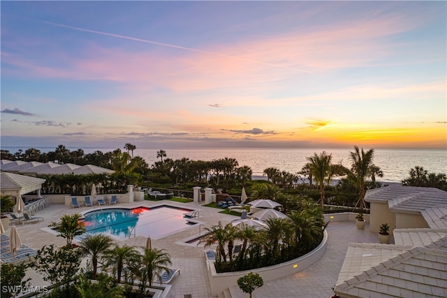 pool at dusk featuring a water view and a patio