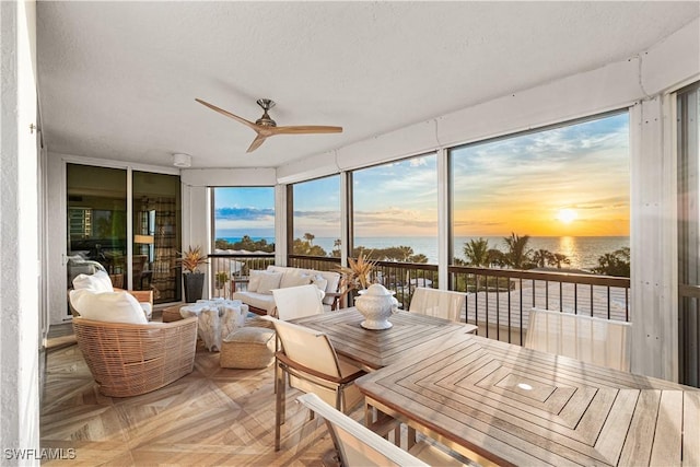 sunroom with ceiling fan and a water view