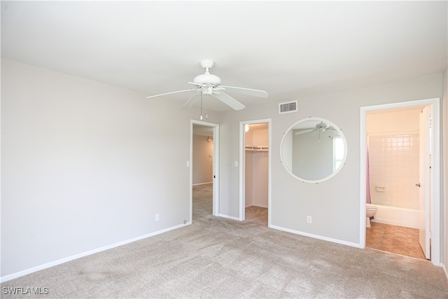 unfurnished bedroom featuring a closet, light carpet, ensuite bath, a walk in closet, and ceiling fan