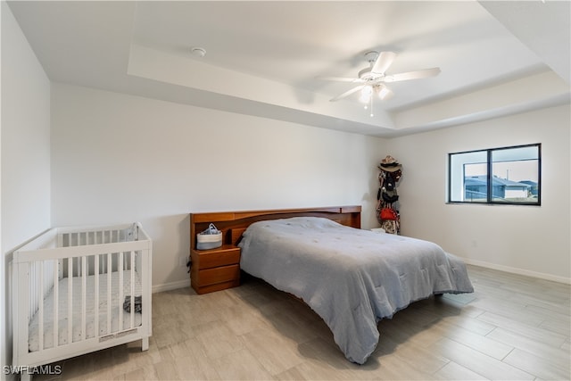 bedroom featuring light wood-type flooring, a raised ceiling, and ceiling fan