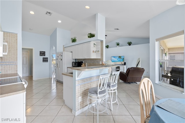 kitchen featuring white cabinets, light tile patterned floors, kitchen peninsula, a kitchen breakfast bar, and vaulted ceiling