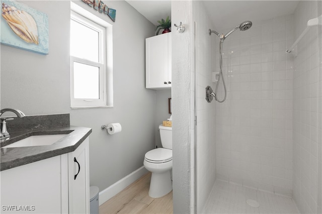 bathroom with toilet, vanity, wood-type flooring, and a tile shower