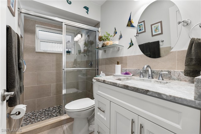 bathroom featuring a shower with door, tile patterned flooring, vanity, toilet, and tile walls