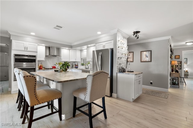 kitchen with light hardwood / wood-style floors, white cabinetry, appliances with stainless steel finishes, crown molding, and wall chimney range hood