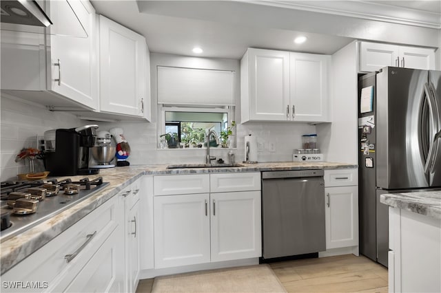 kitchen with stainless steel appliances, white cabinetry, backsplash, sink, and light hardwood / wood-style flooring