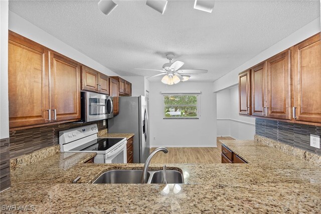 kitchen with appliances with stainless steel finishes, decorative backsplash, ceiling fan, light hardwood / wood-style flooring, and sink